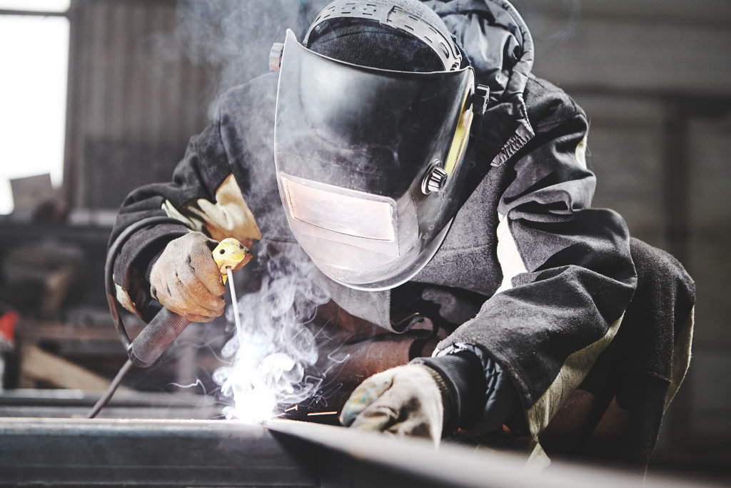 Welder working on metal frames in an industrial plant without a fume extractor.